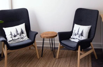 Two dark grey armchairs with tree-design pillows and a wooden table.