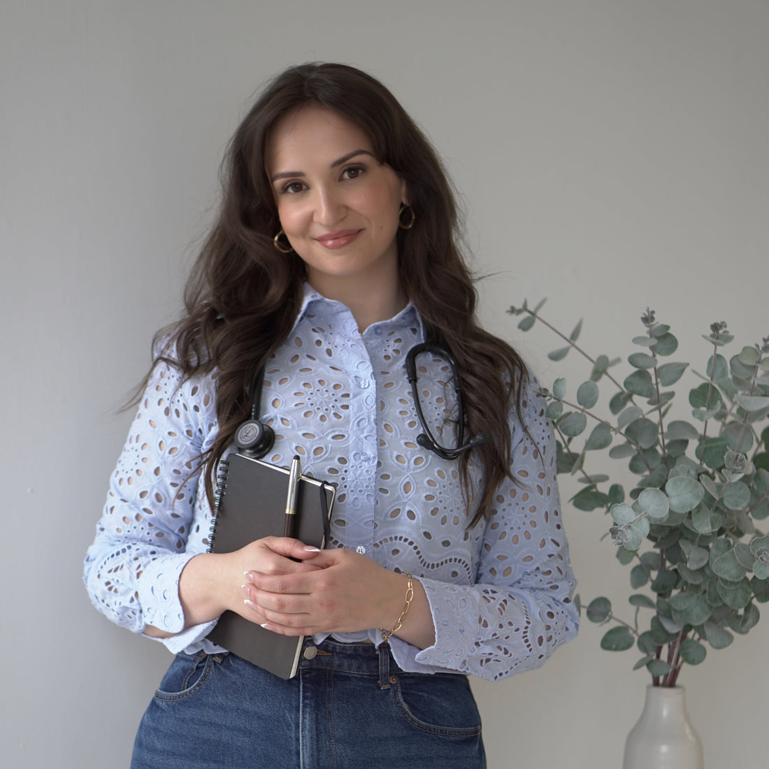 Woman holding a notebook and wearing suspenders in a minimalistic room.