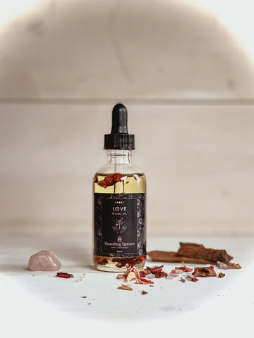 Bottle of 'LOVE' tincture with a dropper on a white surface with dried herbs and crystals. 